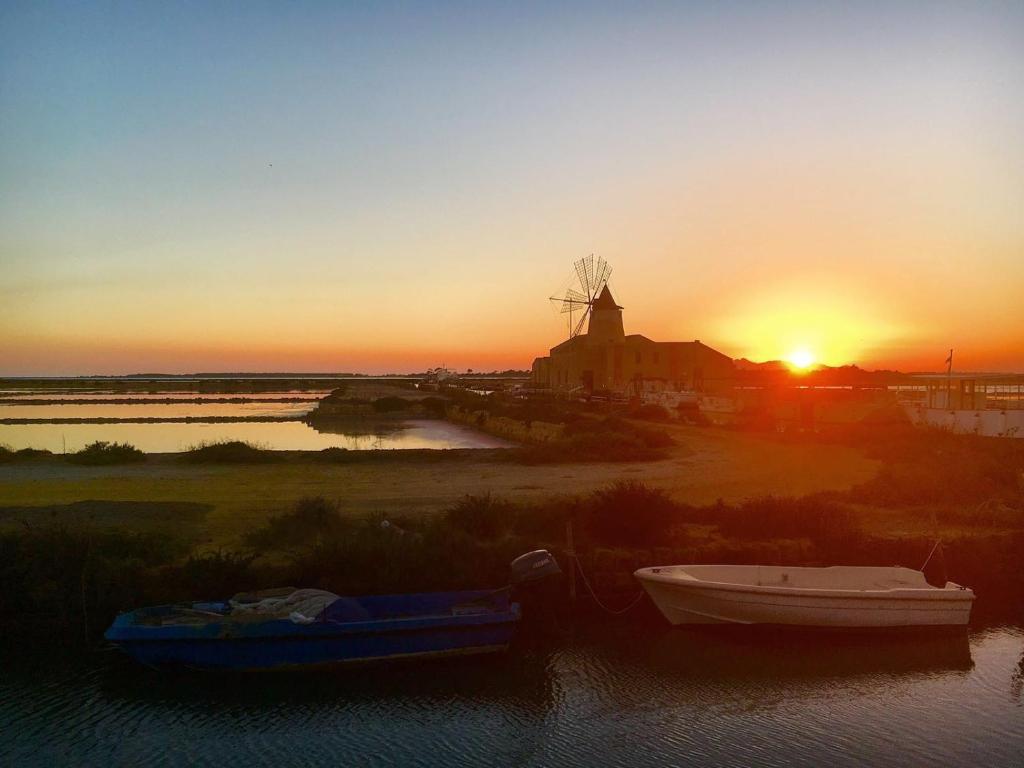 a sunset with two boats in the water with a windmill at The blue house in Marsala