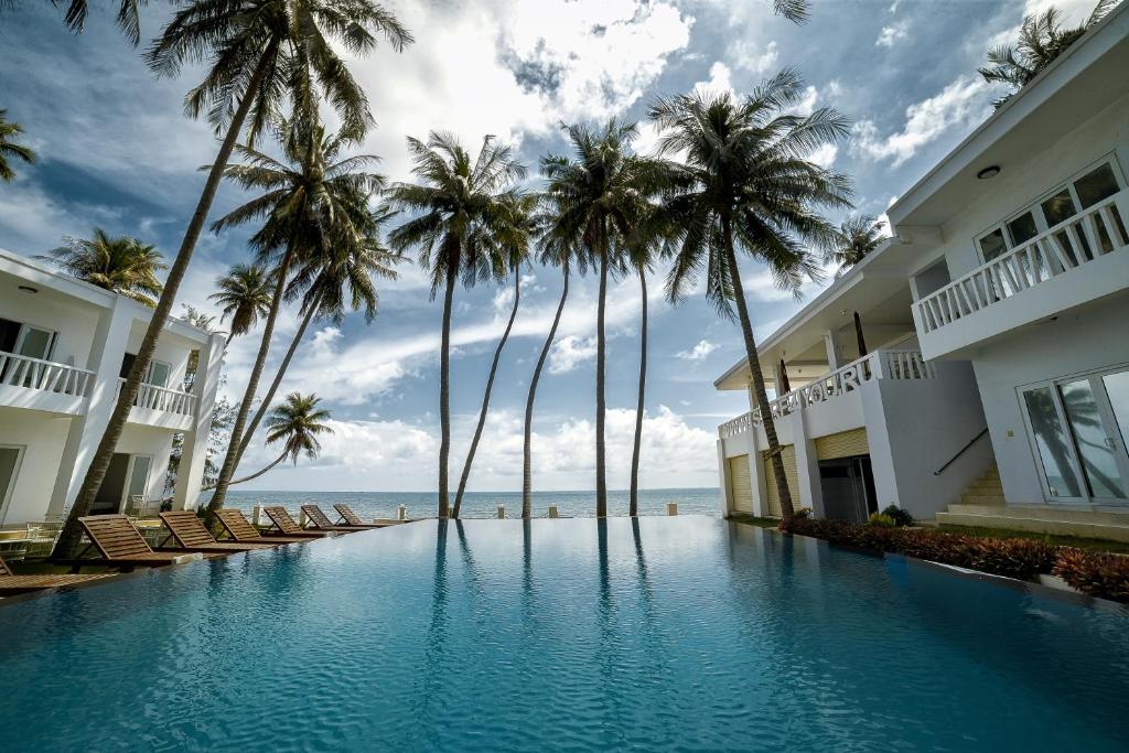 a resort swimming pool with palm trees and the ocean at Surf4You Residence in Mui Ne