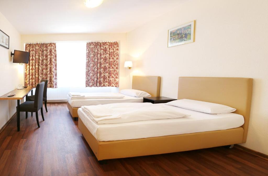 a hotel room with three beds and a desk at Pension Alpha - Frankfurt City Central Station in Frankfurt