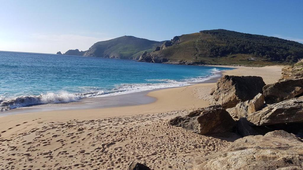 una playa de arena con rocas y el océano en Atico Langosteira, en Finisterre