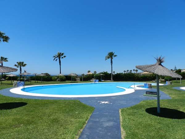 a large swimming pool with an umbrella and grass at Apartamento Atlanterra Bajo in Zahara de los Atunes