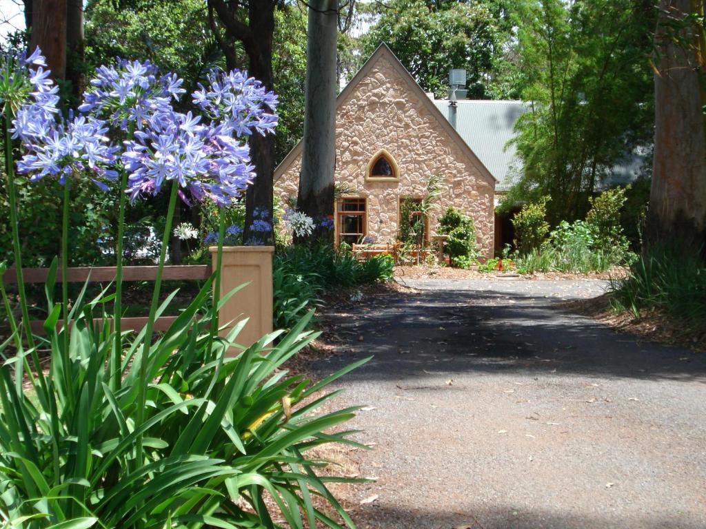 un jardín con flores púrpuras frente a un edificio de piedra en Witches Falls Cottages en Mount Tamborine