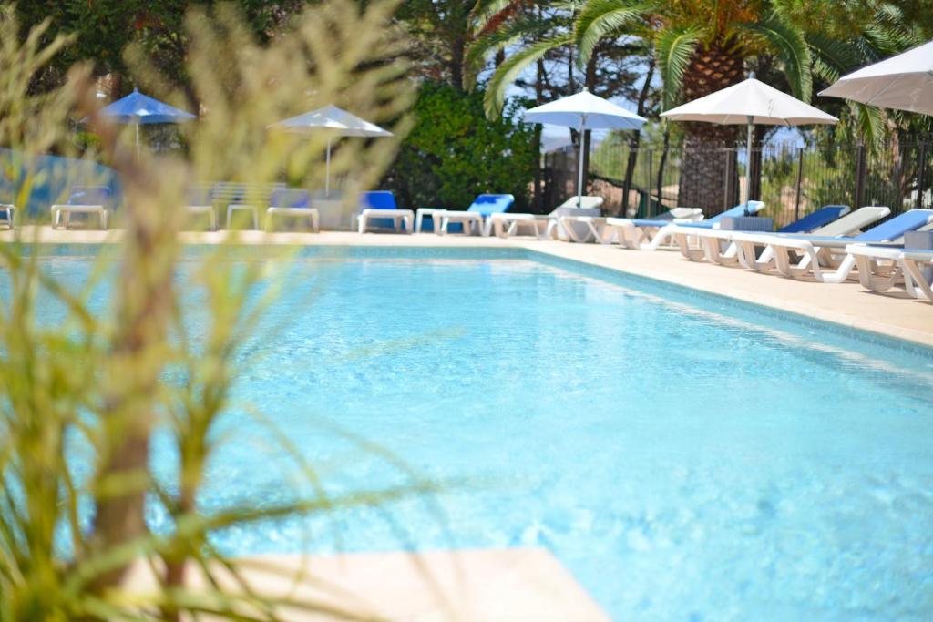 a swimming pool with chairs and umbrellas at Résidence Les Pins in Calvi