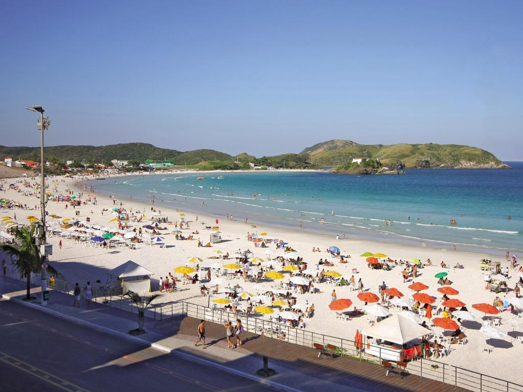 una folla di persone su una spiaggia con ombrelloni di Malibu Palace Hotel a Cabo Frio