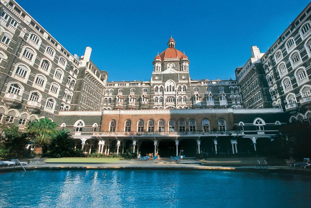 - un grand bâtiment avec une piscine d'eau en face dans l'établissement The Taj Mahal Palace, Mumbai, à Mumbai