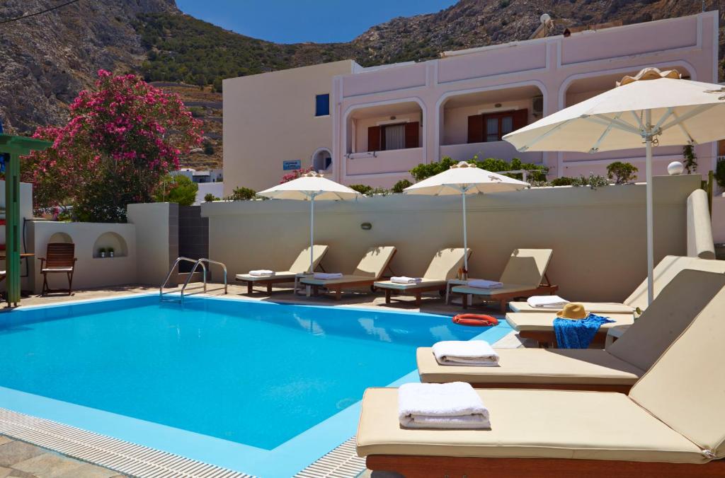 a pool with chairs and umbrellas next to a building at Studios Marios in Kamari