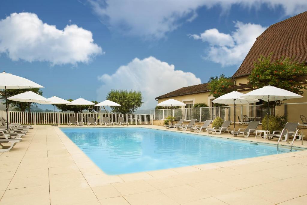 a large swimming pool with chairs and umbrellas at L'Oustal de Vézac in Vézac