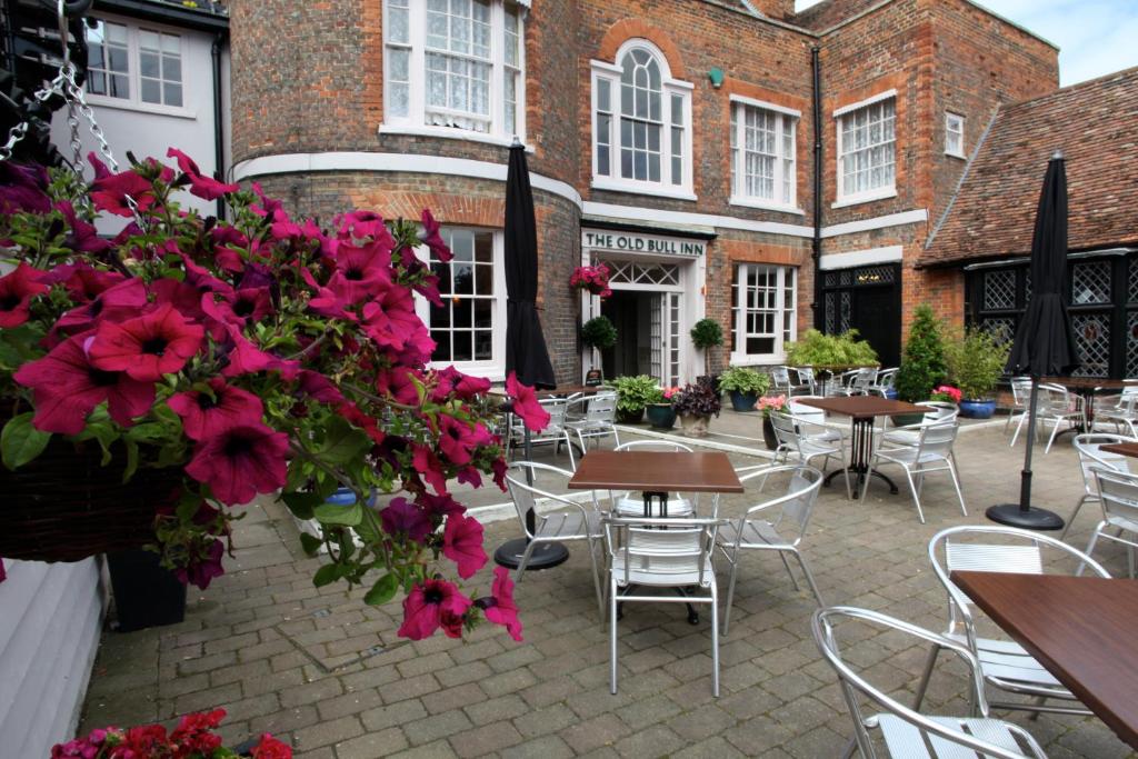 un patio con mesas, sillas y flores rojas en Old Bull Inn, en Royston