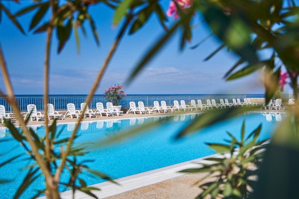 a swimming pool with chairs and the ocean in the background at Apartments Savudrija Plava Laguna in Savudrija