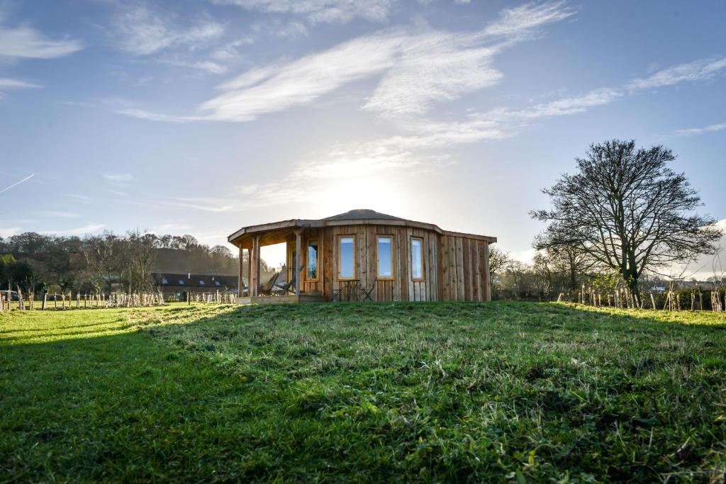 una pequeña casa en un campo con el sol en el cielo en Nether Farm Roundhouses, en Ashbourne