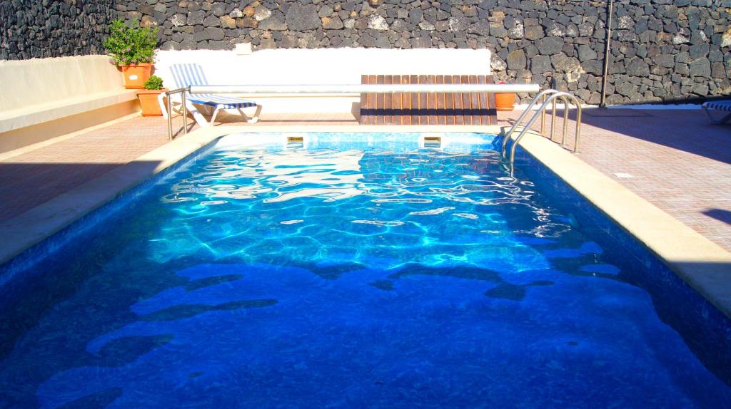 uma piscina com um banco e água azul em Finca la Rubina em Mozaga