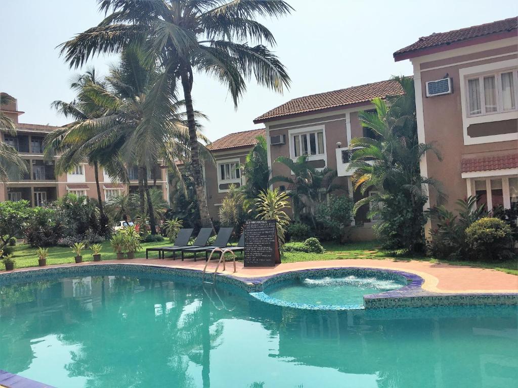 a swimming pool in front of a building with palm trees at 1 BHK Deluxe Apartment in Candolim by GR Stays in Candolim