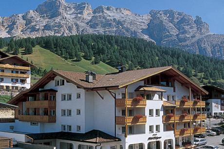a large white building with a mountain in the background at Hotel Falzares in San Cassiano