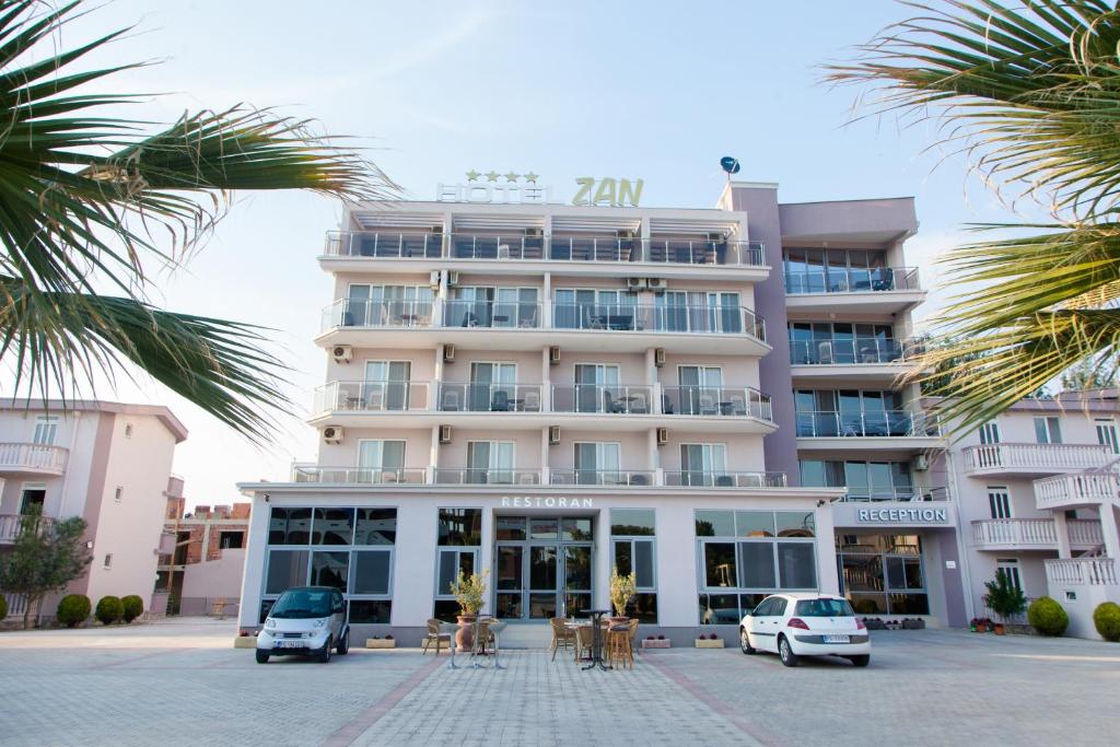 een groot wit gebouw met tafels en stoelen op een parkeerplaats bij Hotel Zan in Ulcinj