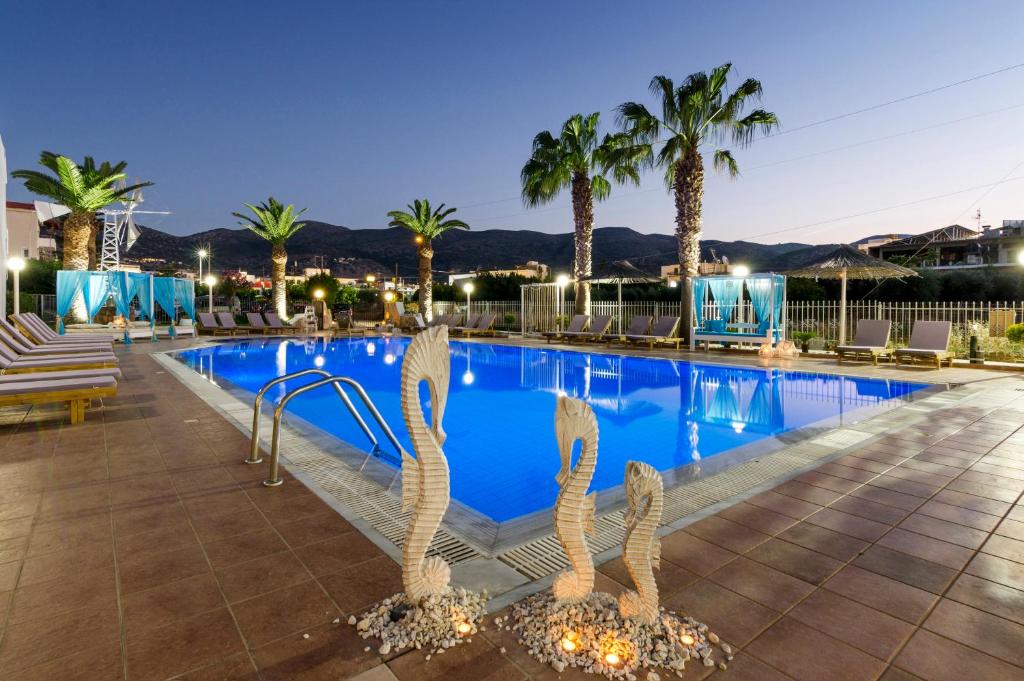 a pool at night with palm trees and a statue at Stelios Gardens in Malia