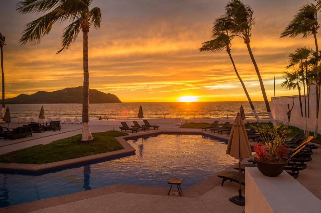 a pool at the beach with a sunset in the background at Ocean View Beach Hotel in Mazatlán