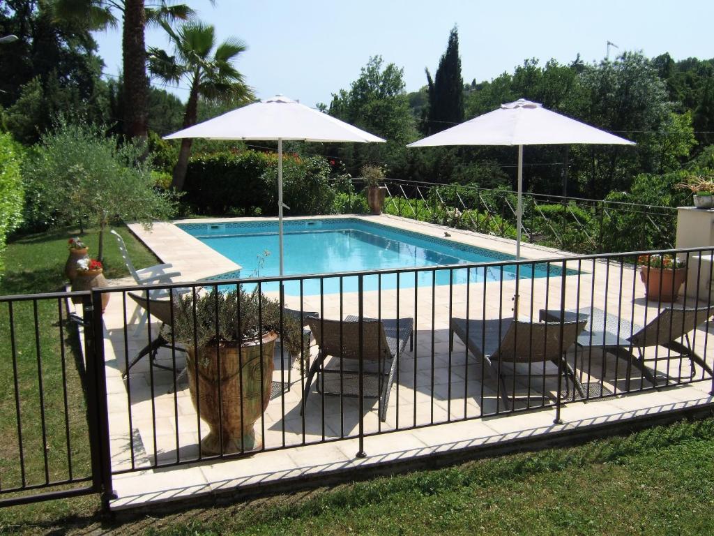 uma piscina com cadeiras e guarda-sóis ao lado de uma cerca em AU VALLON ROUGE (Studio) em Saint-Paul-de-Vence