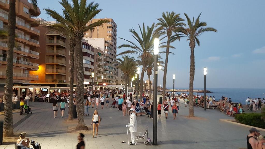 una multitud de personas caminando por una playa con palmeras en Apartamento Torrevieja en Torrevieja