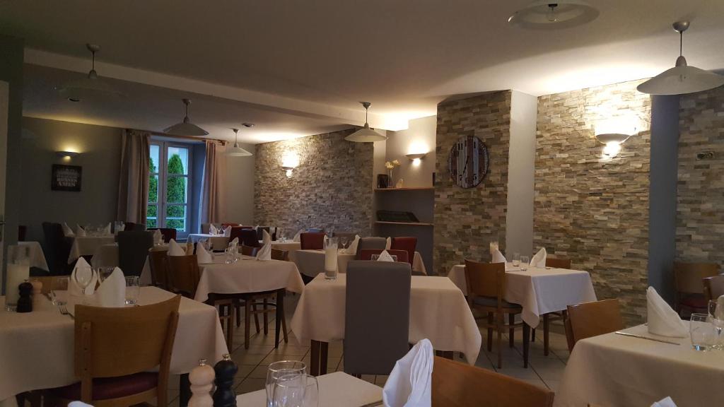 Auberge le Cheylet في Apchon: مطعم بطاولات بيضاء وكراسي وجدران من الطوب