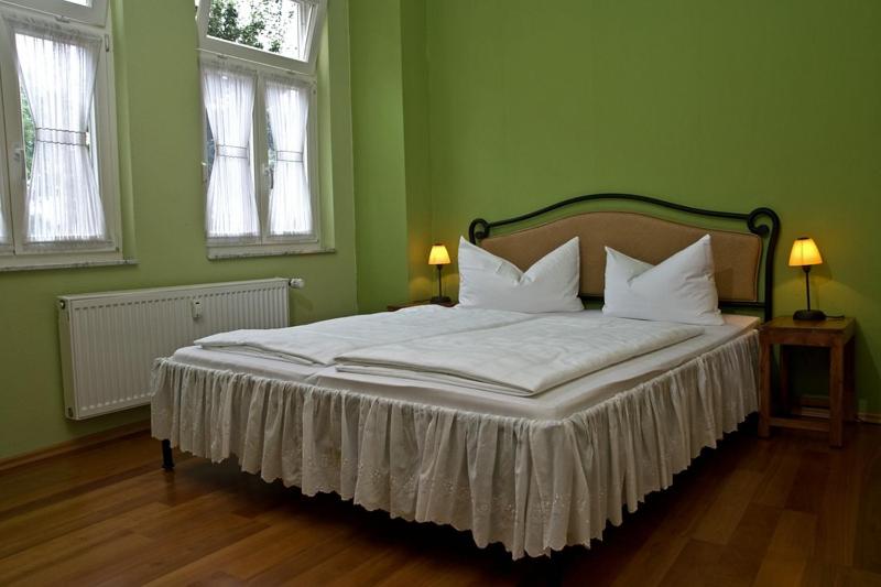 a bed in a green bedroom with two windows at Am Kleinsten Haus in Wernigerode