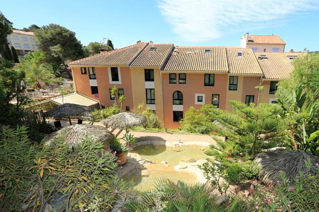 un grand bâtiment avec un jardin en face dans l'établissement Hotel Residence Les Medes, à Porquerolles