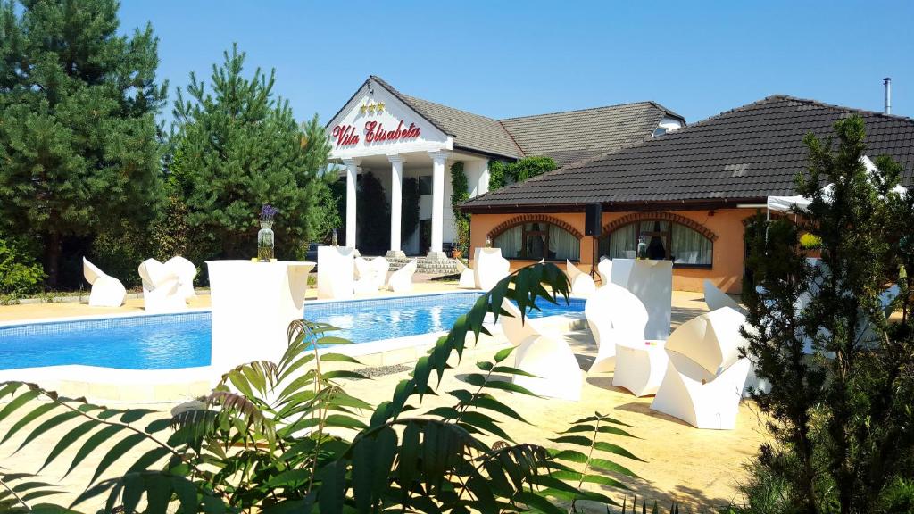 a pool with white chairs in front of a building at Hotel Elisabeta in Alba Iulia