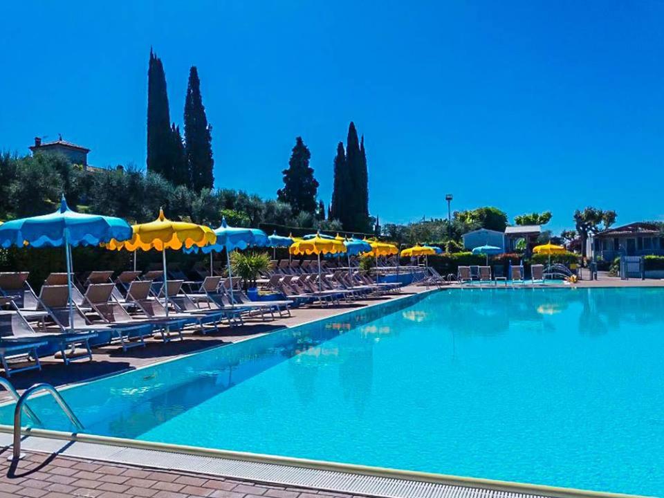 uma grande piscina com cadeiras e guarda-sóis em Camping Serenella em Bardolino