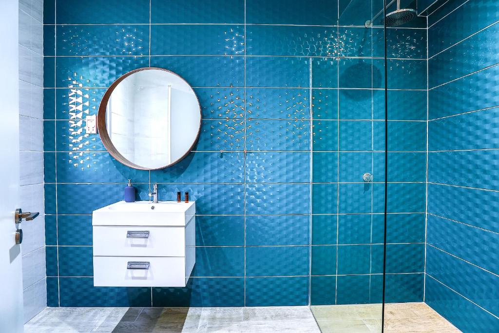 Baño de azulejos azules con espejo y lavabo en Vega Apartments, en Limassol