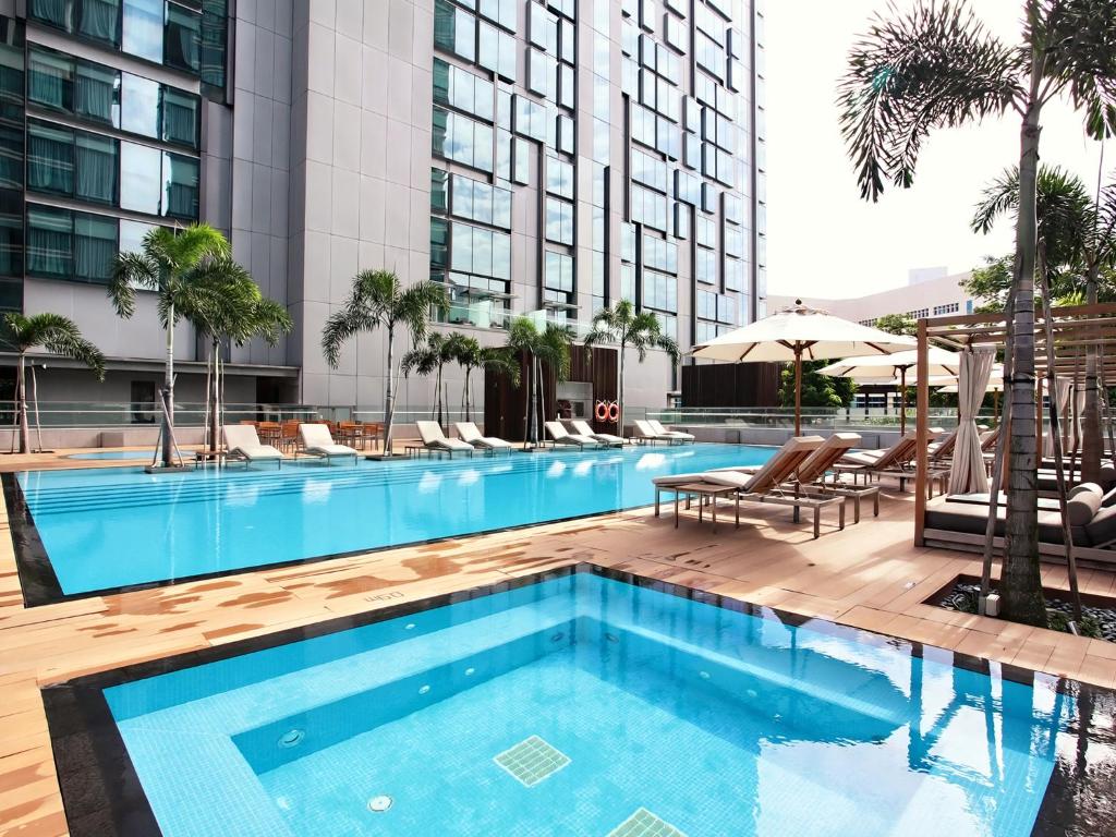 Oasia Hotel Novena, Singapore by Far East Hospitality في سنغافورة: مسبح وكراسي وطاولة ومبنى