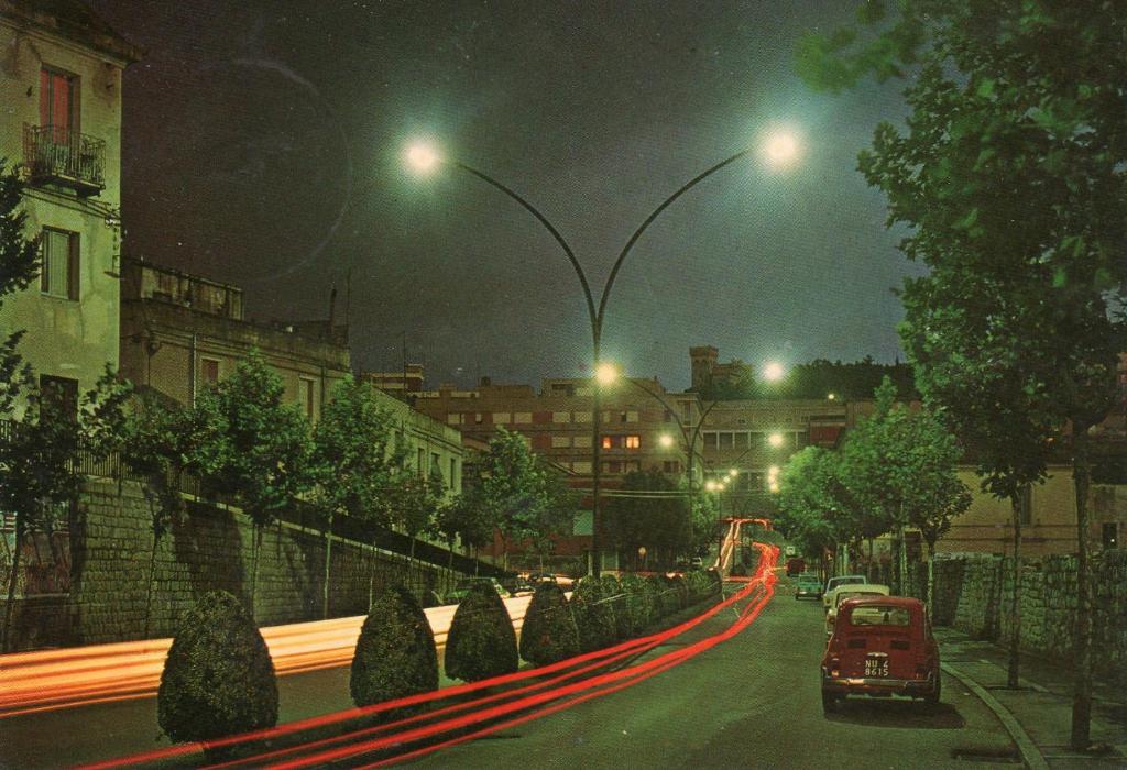 una strada di città di notte con macchine e lampioni di Da Tore a Nuoro