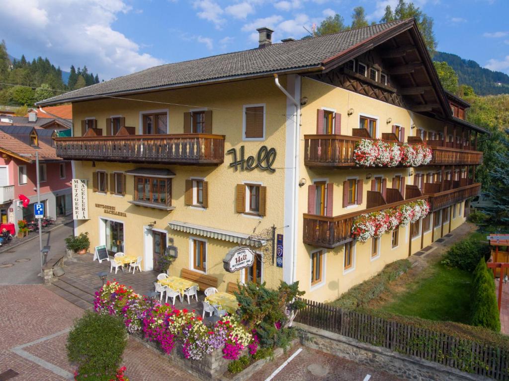 ein großes gelbes Gebäude mit Balkonen, Tischen und Blumen in der Unterkunft Hotel Hell in Welsberg-Taisten