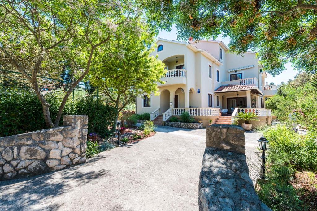 a large white house with a stone wall at Apartments Rozelyn in Ugljan