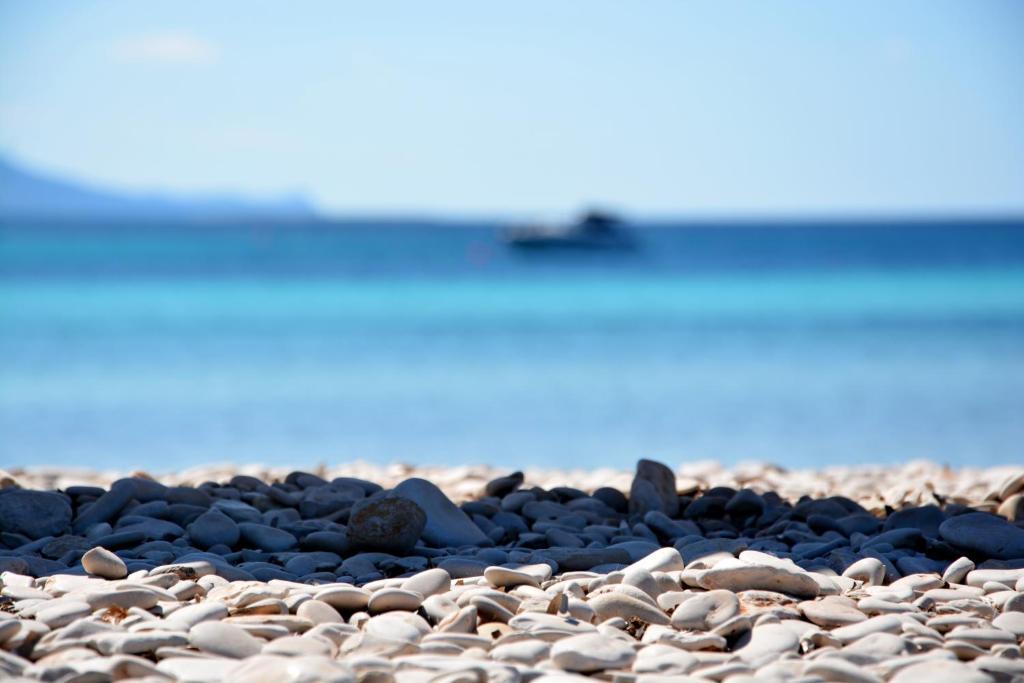 a group of rocks on a beach with a boat in the background at Apartments Marta in Verunić
