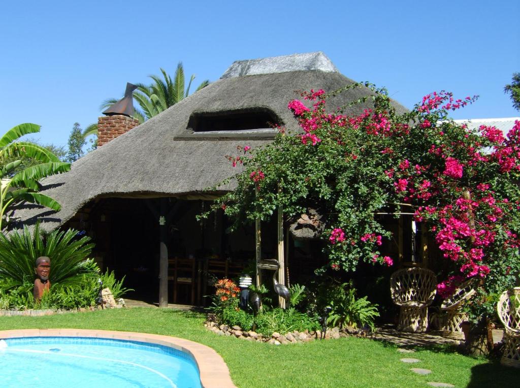 une maison au toit de chaume avec une piscine en face de celle-ci dans l'établissement African Kwela Guest House, à Windhoek