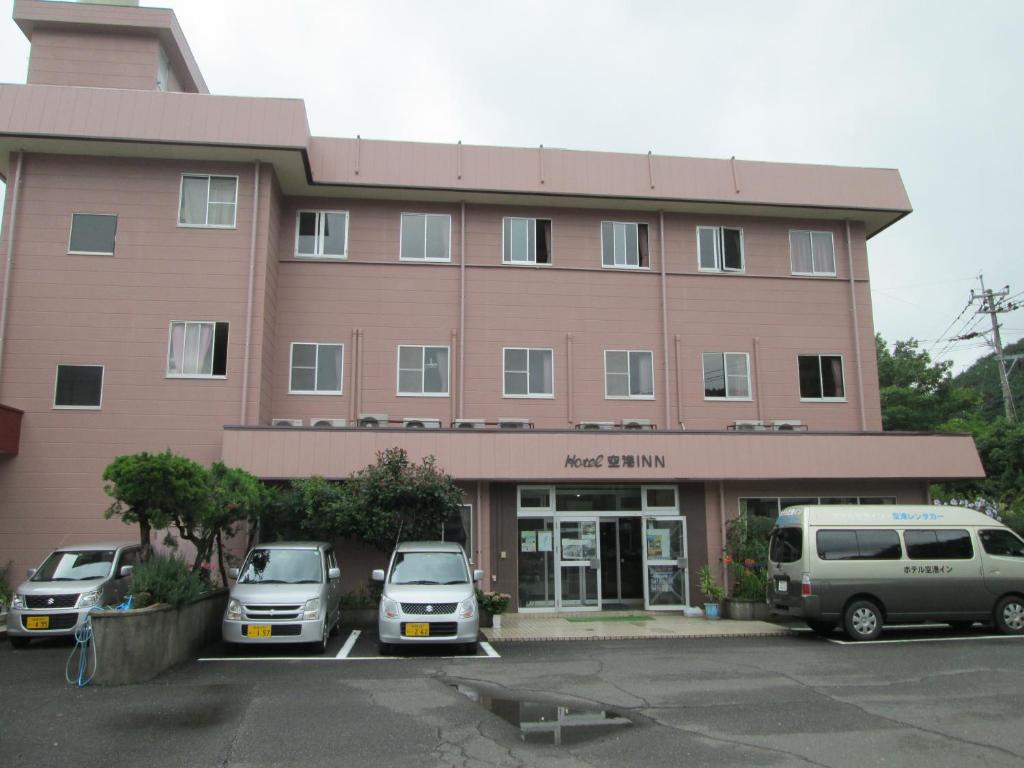 Hotel Kuko Inn في تسوشيما: مبنى به سيارتين متوقفة في موقف للسيارات
