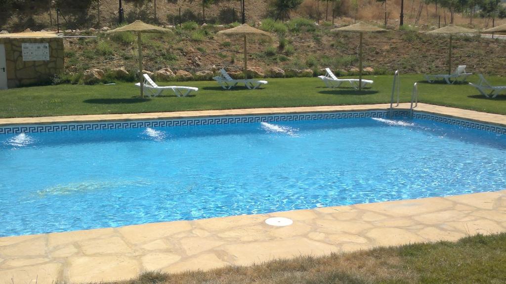 a large swimming pool with two lawn chairs and umbrellas at Complejo Pueblo Blanco in Olvera
