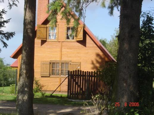 a brown house with a fence and two trees at Domki letniskowe "Kosówka" in Łeba