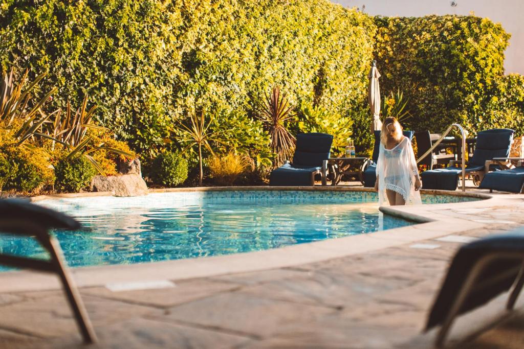 a woman standing next to a swimming pool with an umbrella at The Club Hotel & Spa Jersey in Saint Helier Jersey