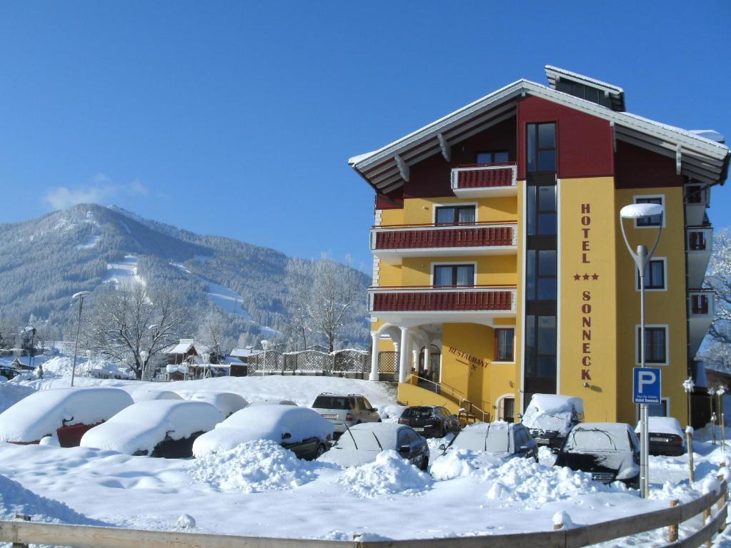 ein schneebedecktes Gebäude mit Autos auf einem Parkplatz in der Unterkunft Hotel Sonneck in Schladming