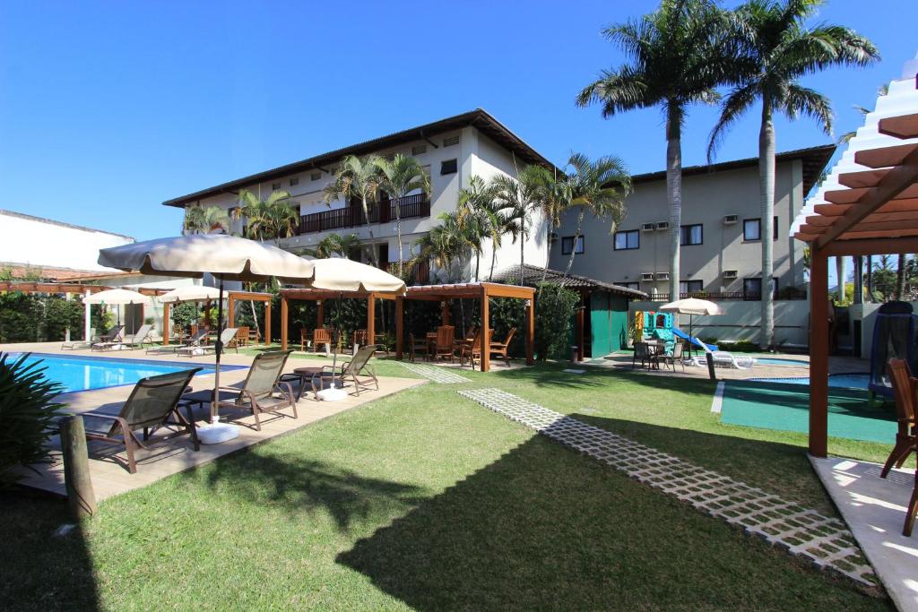 uma piscina com cadeiras e guarda-sóis ao lado de um edifício em Hotel Ilhas do Caribe - Na melhor região da Praia da Enseada no Guarujá