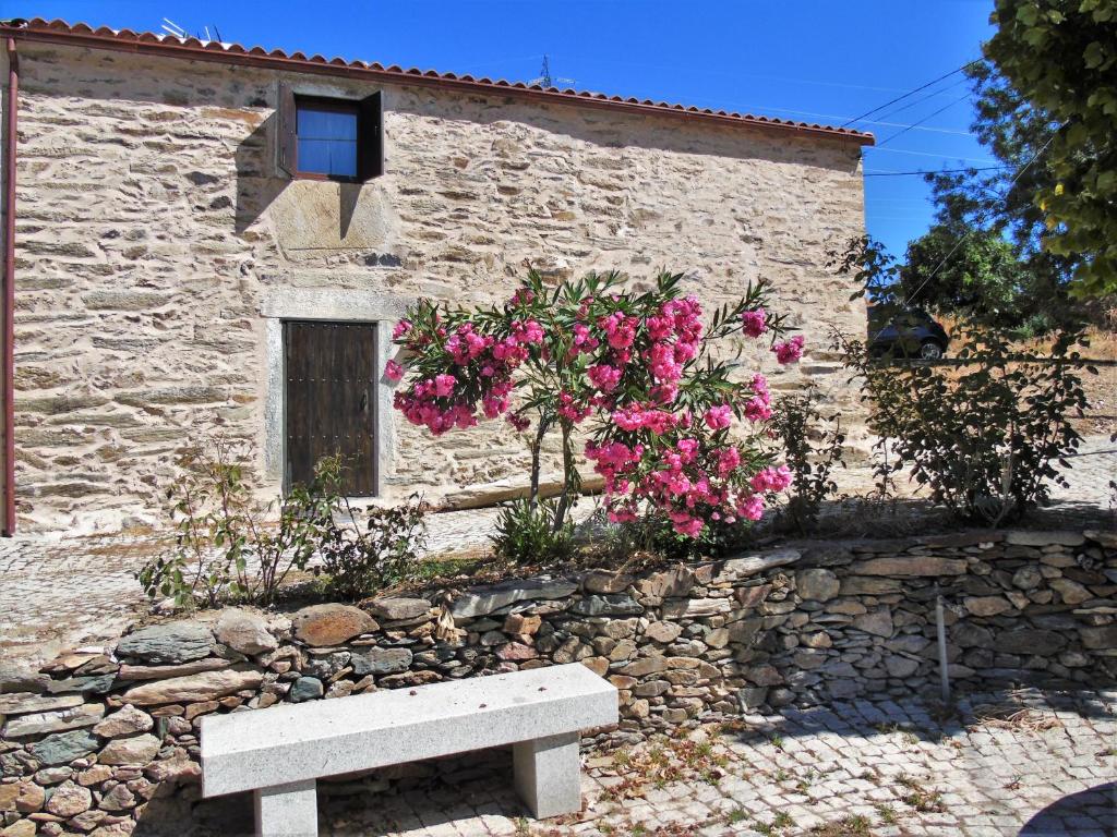 a bench in front of a stone building with pink flowers at Casas de Xisto in Mogadouro