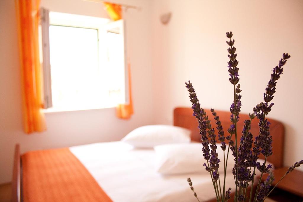 1 dormitorio con cama, ventana y mesa con flores en Apartments Jaksic, en Postira