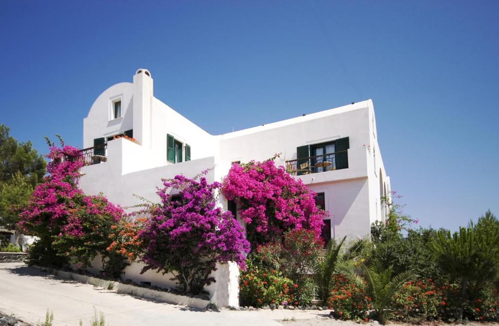 une maison blanche avec des fleurs violettes devant elle dans l'établissement Costa Marina Villas, à Fira