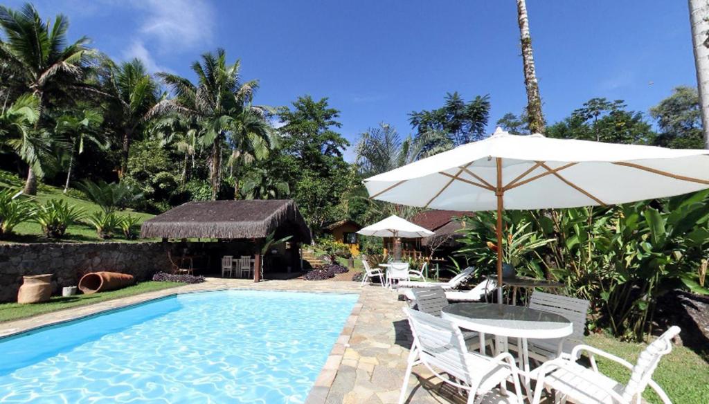a pool with a table and an umbrella and chairs at Pousada Bromélias in Paraty