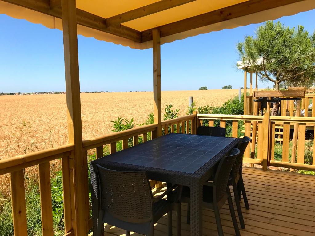 a table and chairs on a deck with a view of a field at Camping Paradis 4 étoiles Au Port de L'Houmeau - La Rochelle in LʼHoumeau