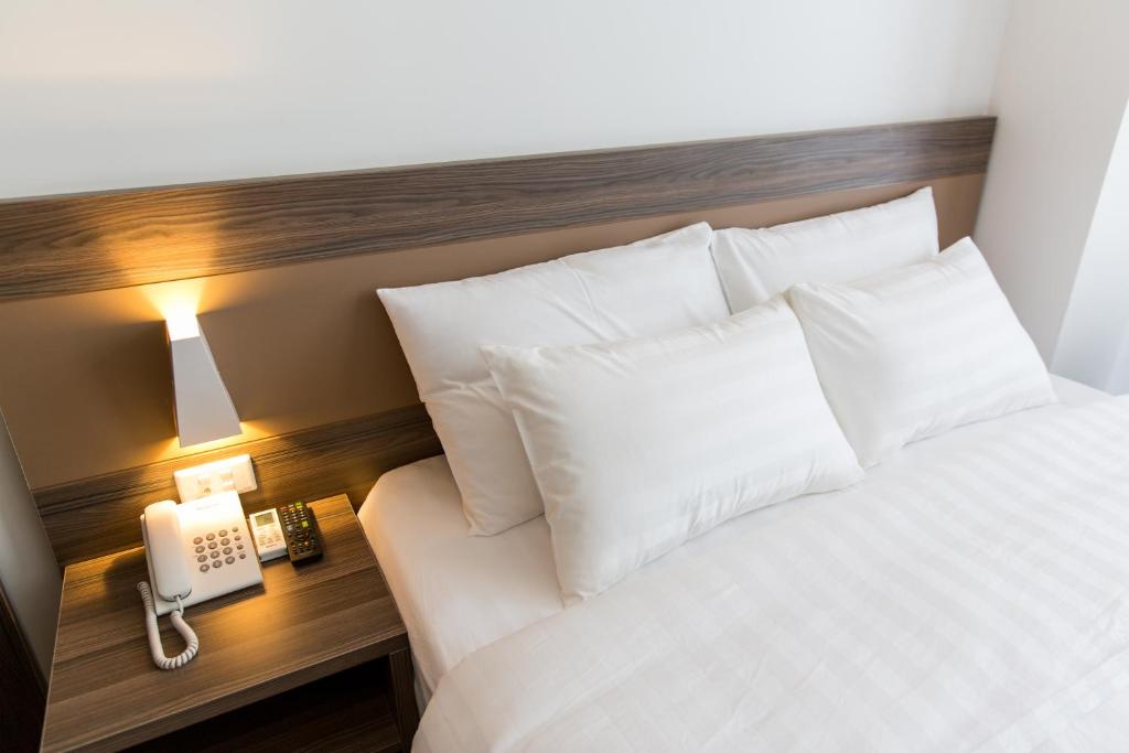 a bed with white pillows and a phone on a table at Punt Hotel in Hai Phong