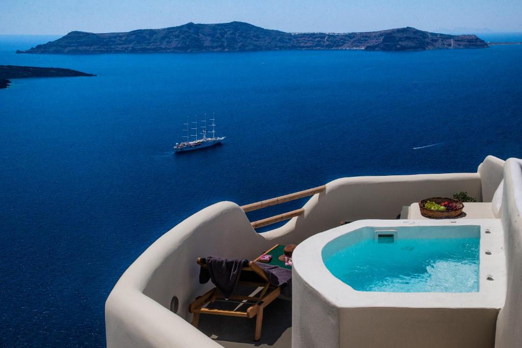 a balcony with a swimming pool and a boat in the water at Aperto Suites - Adults Only in Fira