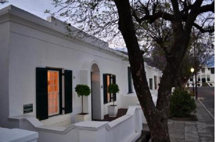 ein weißes Gebäude mit zwei Topfpflanzen davor in der Unterkunft De Kothuize 10 in Graaff-Reinet
