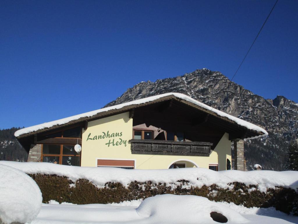 un edificio cubierto de nieve con una montaña en el fondo en Landhaus Hedy, en Heiterwang