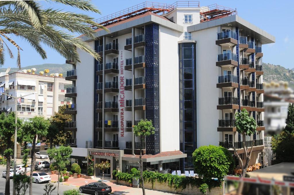 een hoog wit gebouw met palmbomen ervoor bij Kleopatra Micador Otel in Alanya